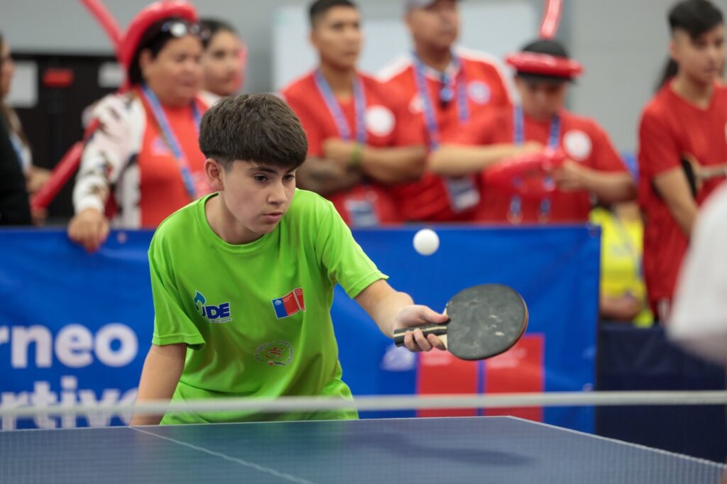 Fotografía de joven con polera verde jugando para tenis de mesa. 