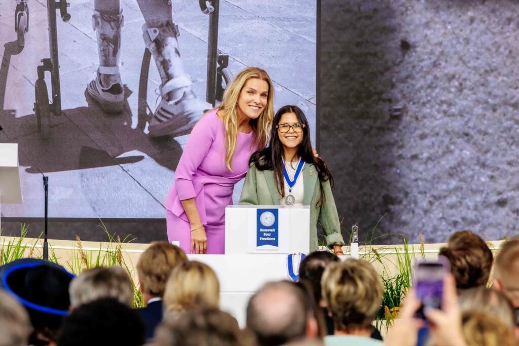Fotografía de Isidora Uribe junto a representante de la fundación detrás de un podio con su medalla en el cuello.