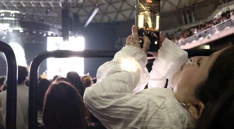 Fotografía de Camila Herrera en su silla de ruedas echada hacia atrás grabado en el concierto de Rosalía con su celular, sobre la plataforma de accesibilidad del Movistar Arena.