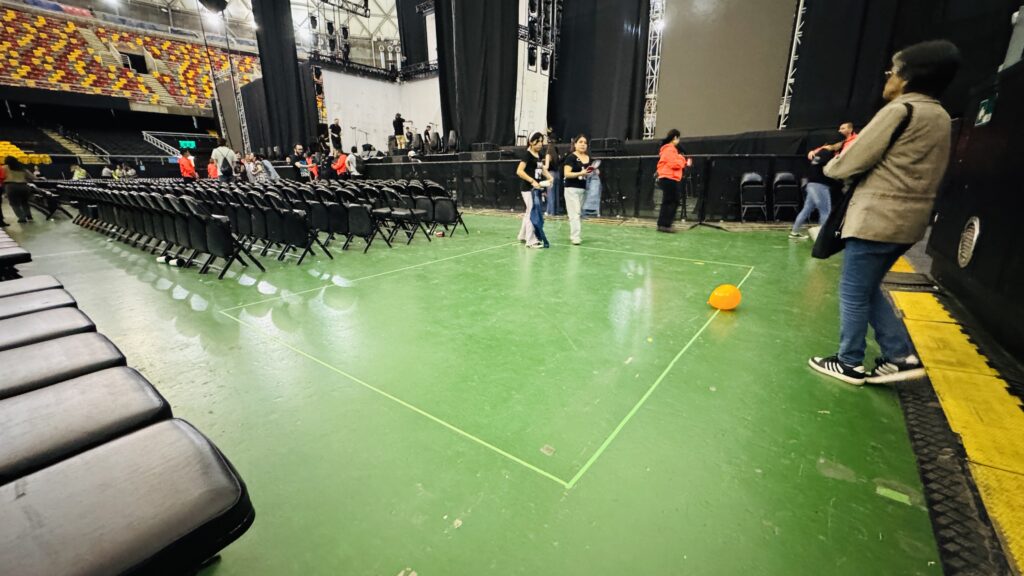 Fotografía del espacio disponible para ubicar a las personas con discapacidad en Movistar Arena cuando se venden cancha numerada. En el suelo está demarcado con cinta un cuadrado al costado de las sillas y junto al escenario. 